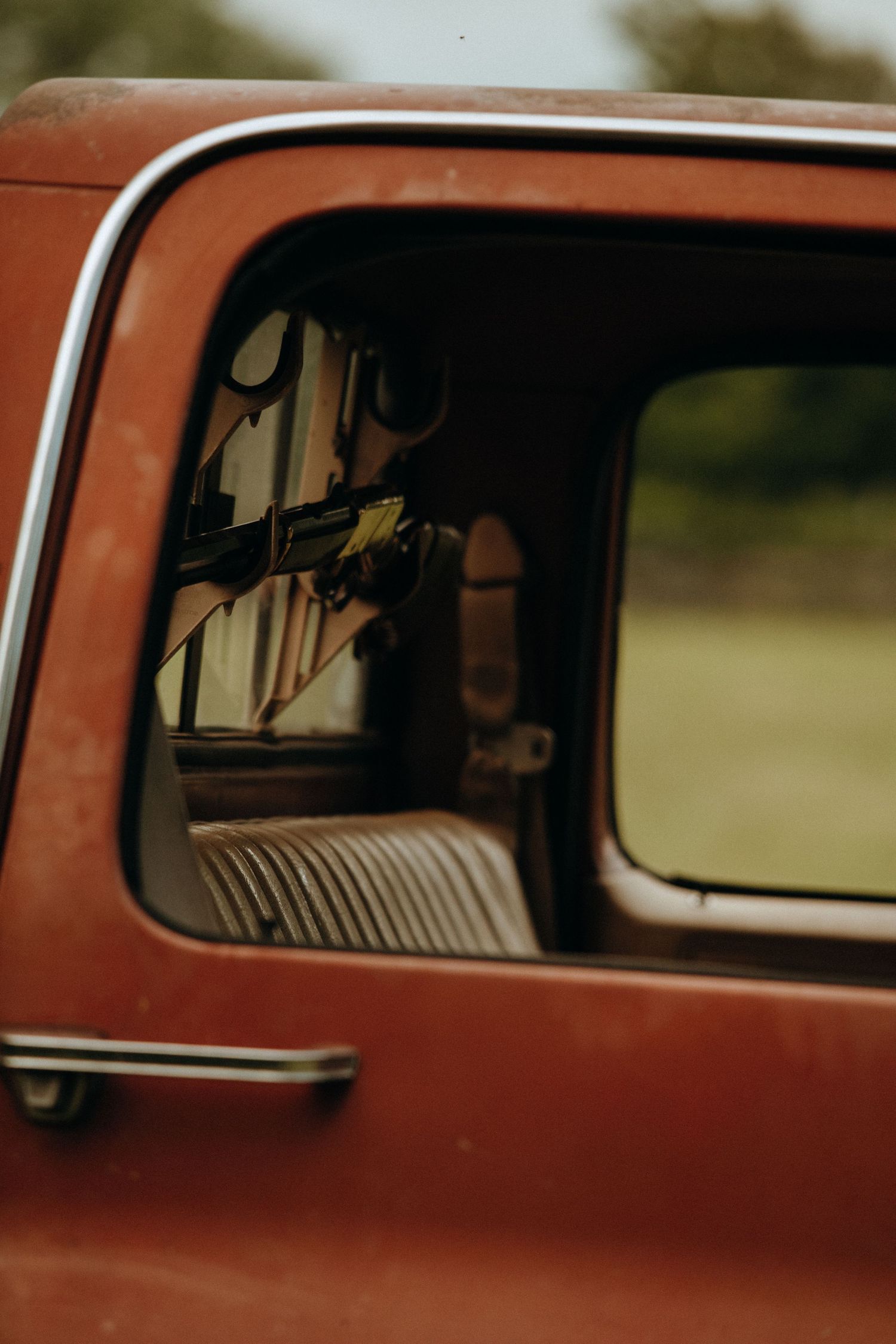 Close-up of a vintage red truck window and door handle with blurred green background outside.