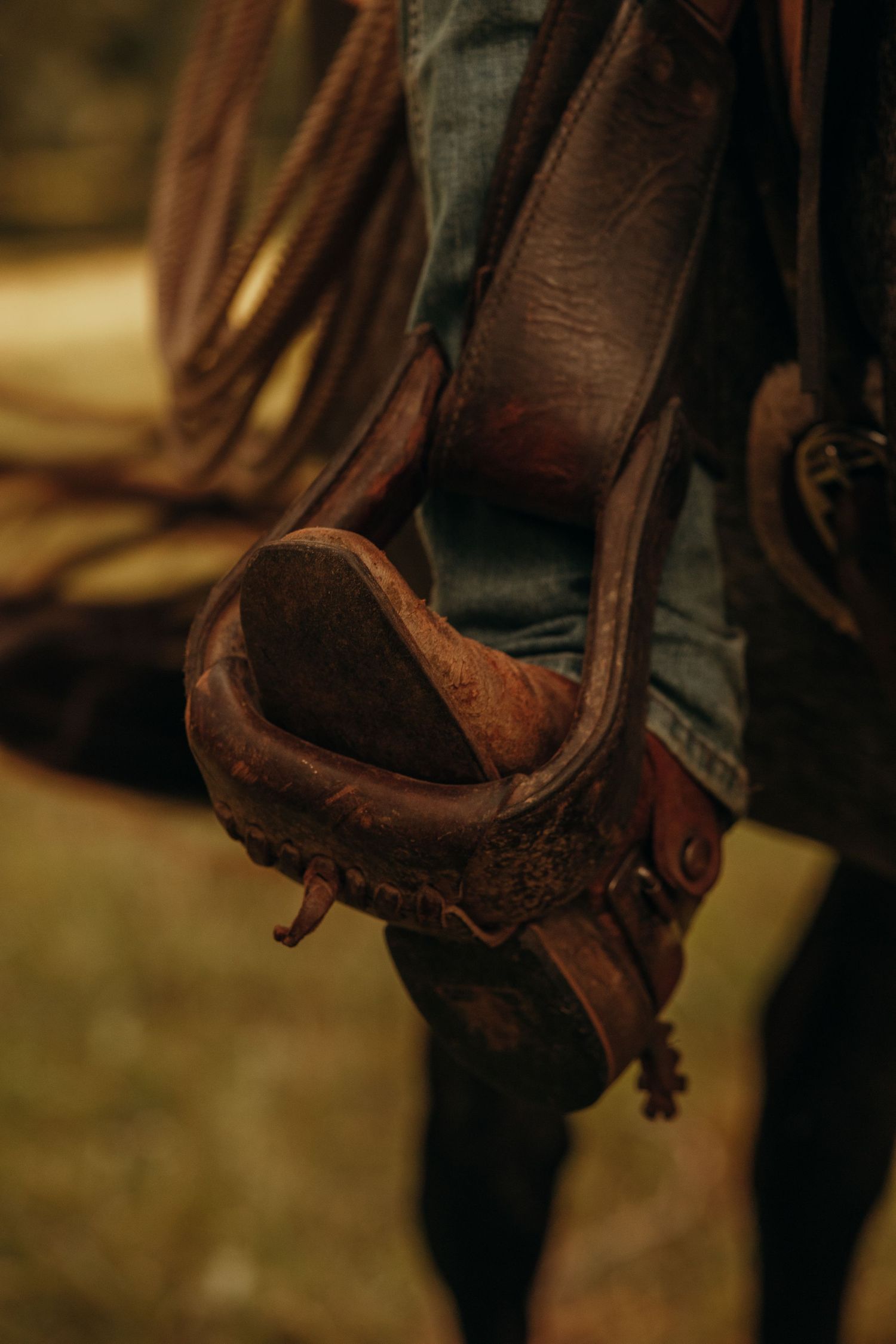 Close-up of worn leather cowboy boot with spur in stirrup against denim jeans on horseback.