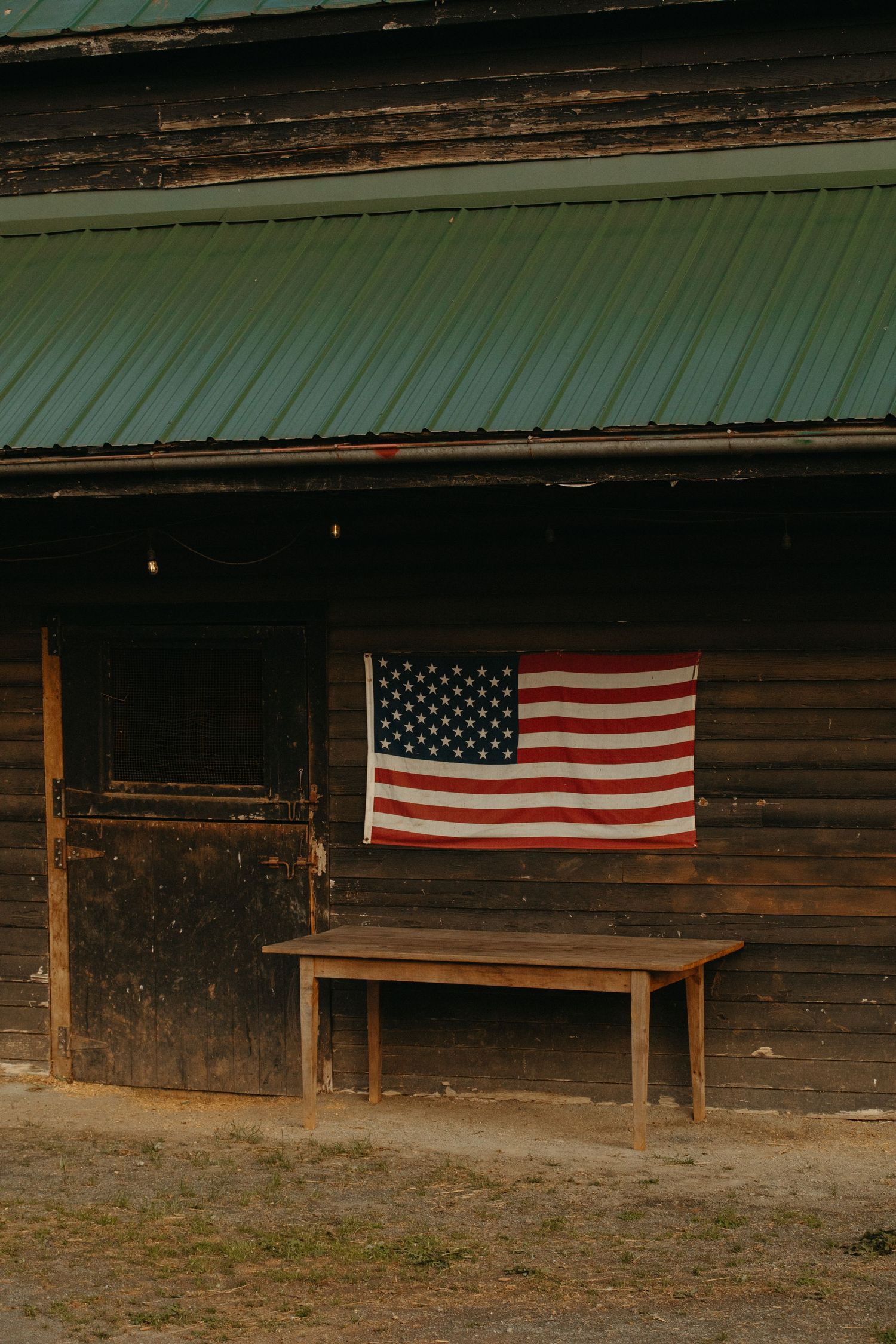 American flag hanging on a rustic wooden barn wall above a wooden bench.