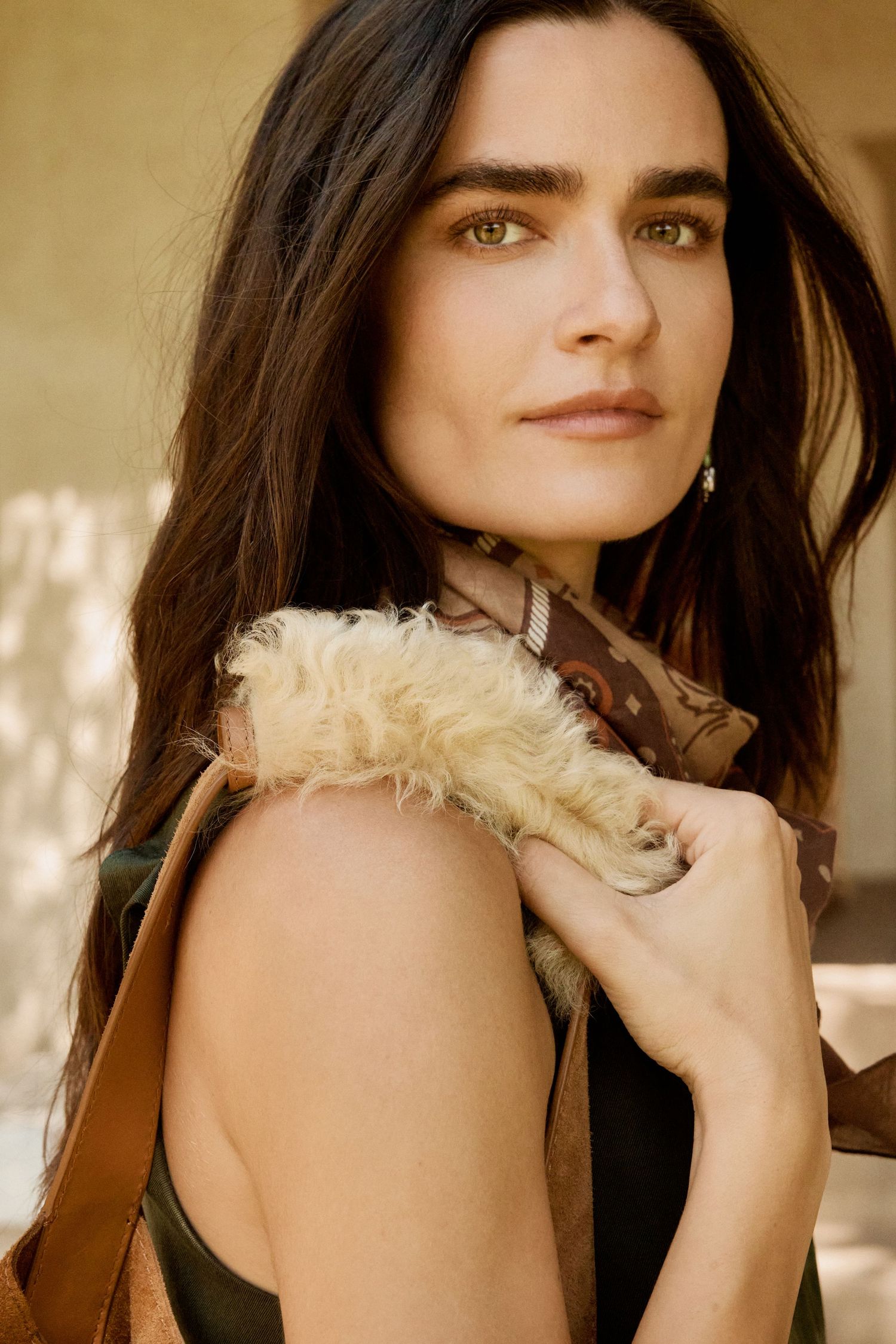 Close-up portrait of dark-haired woman holding a furry accessory with a brown leather bag.