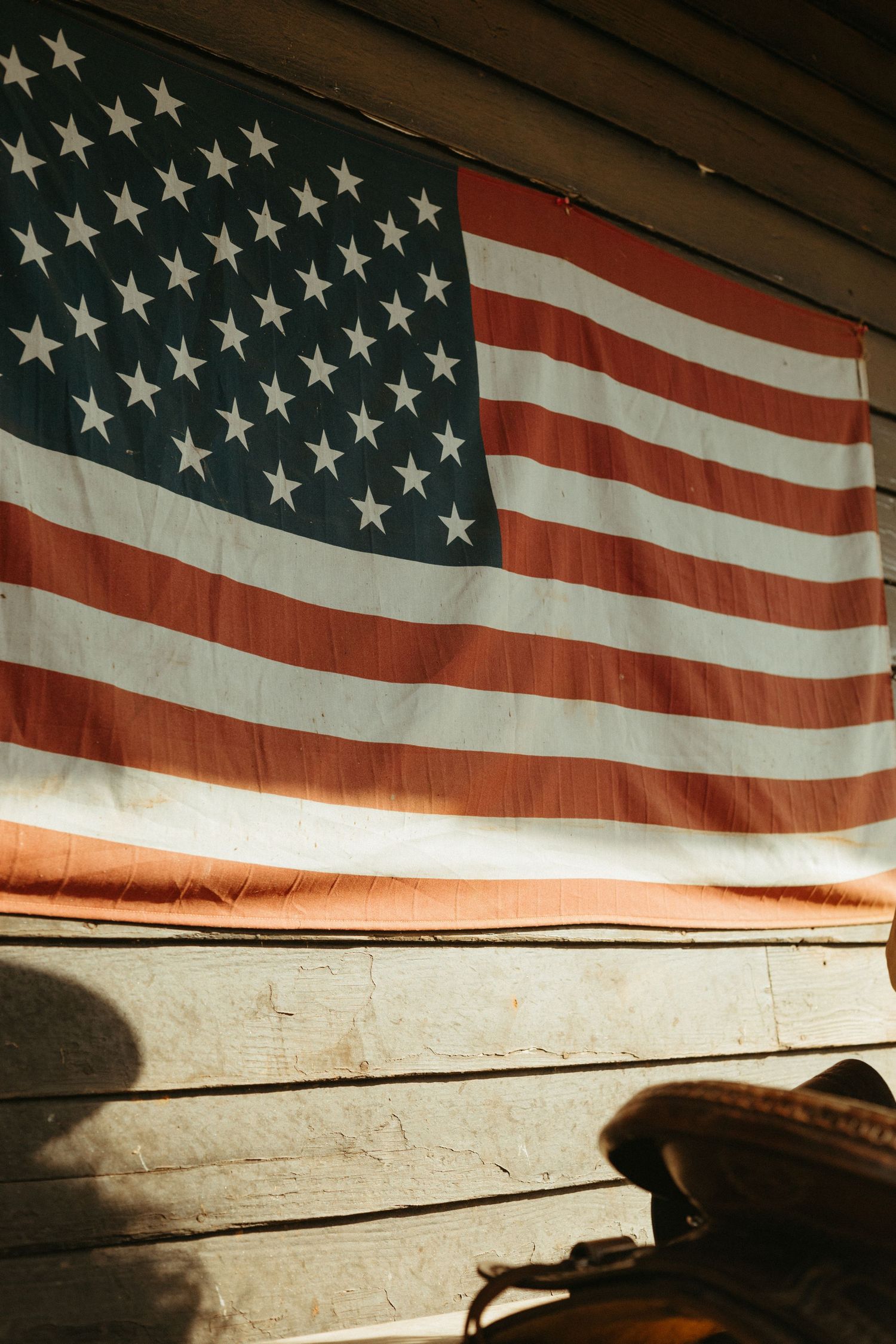 Vintage American flag with stars and stripes hanging on a rustic wooden wall in warm sunlight.