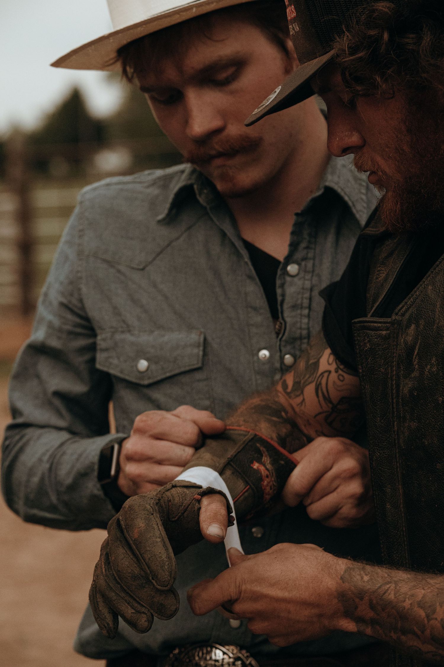 Two cowboys in hats wrapping a wrist with rodeo rope before a bull ride.
