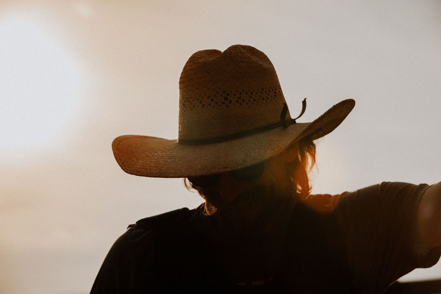 Silhouette of a person wearing a straw cowboy hat backlit by warm golden sunset light.