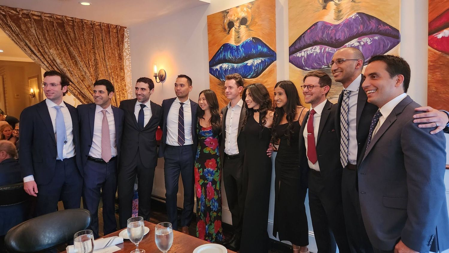Group of elegantly dressed men and women posing together at a formal dinner event in a decorated restaurant.
