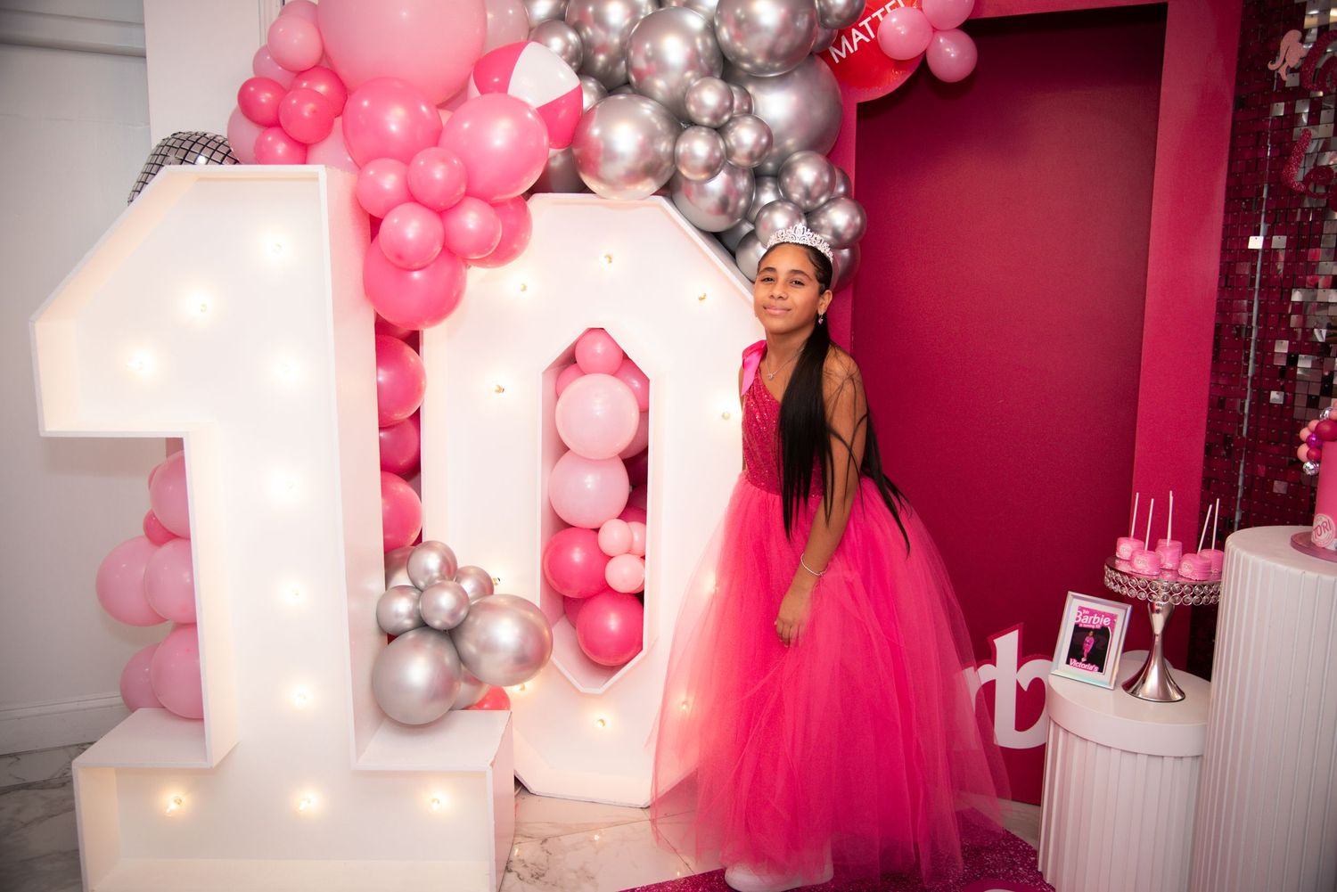 A pink and silver balloon arch decorates a party setup with illuminated number 10 and a bright pink tulle dress by FBM Studios in Ft Lauderd