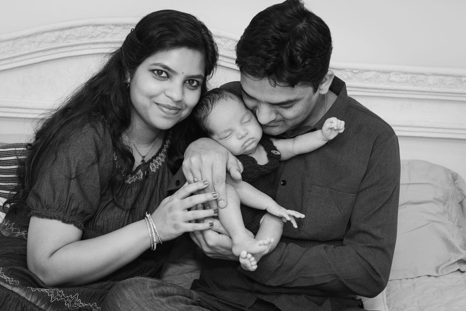Black and white photo of smiling parents holding their newborn baby, family portrait.