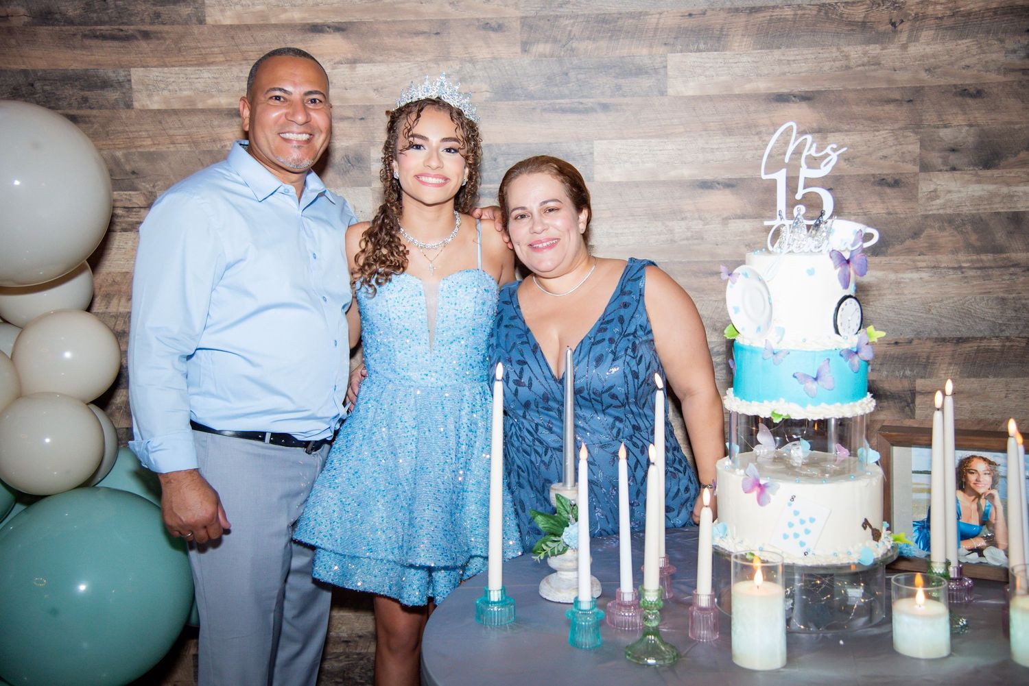 Family posing together at a quinceañera celebration with a decorated cake and candles on a table.