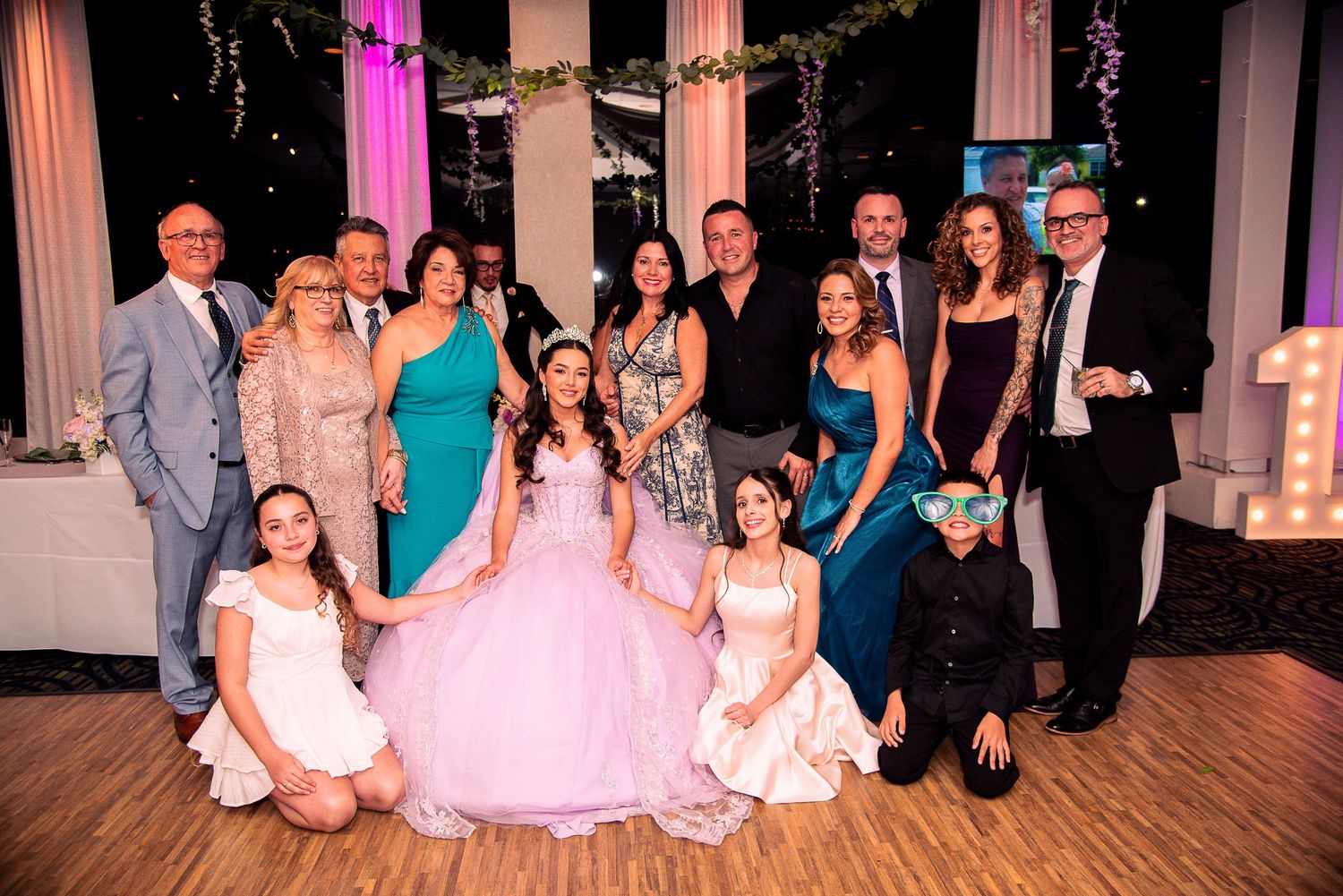 A quinceañera girl in a pink ball gown poses with her large family group at an elegant decorated venue by FBM Studios in Fort Lauderdale Fl