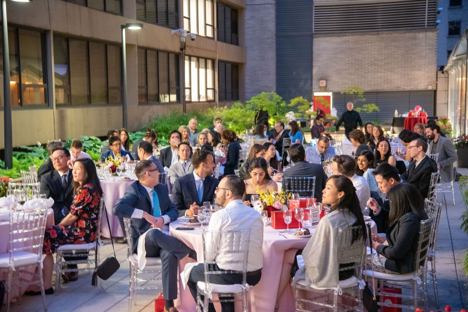Guests enjoy an elegant outdoor banquet dinner at round tables during a formal evening event at an urban venue.