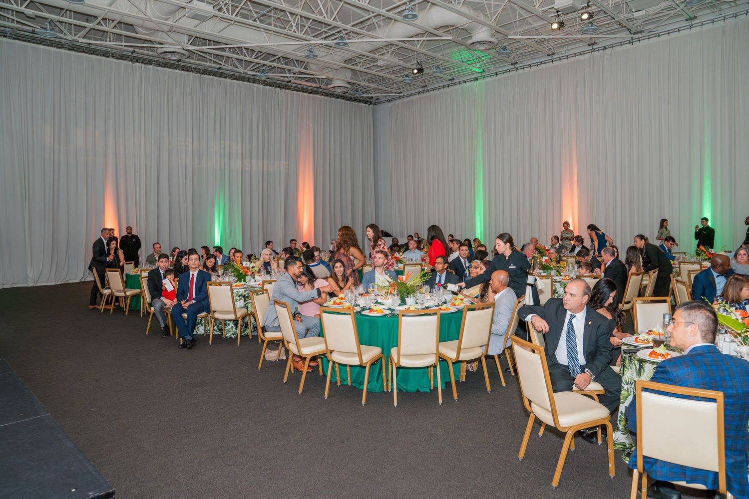 Elegant banquet hall with guests seated at round tables during a formal dinner event with green and pink uplighting.