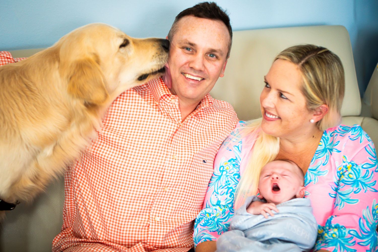 Happy family with newborn baby and golden retriever dog sitting together on a couch at home.