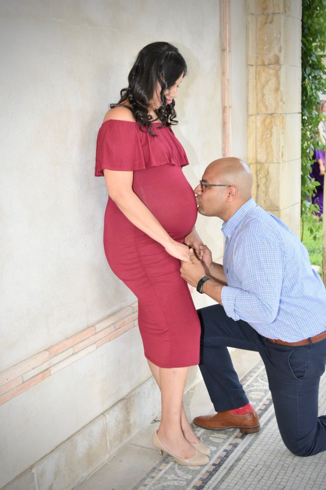 A man kneels to kiss a pregnant woman's belly during a maternity photo shoot outdoors.
