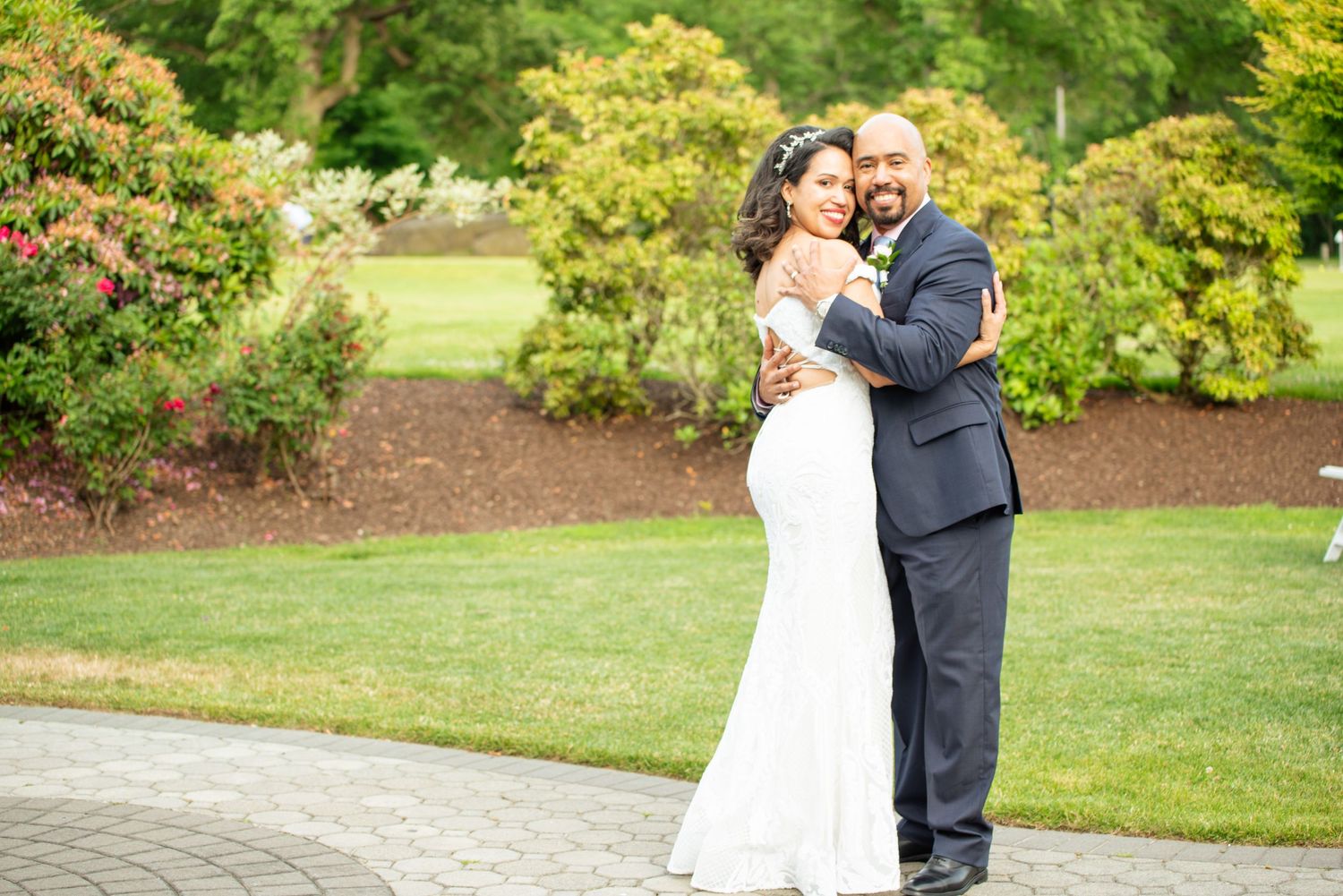 A couple in wedding attire embraces on a stone path surrounded by lush gardens and greenery by FBM Studios in Fort Lauderdale Florida.