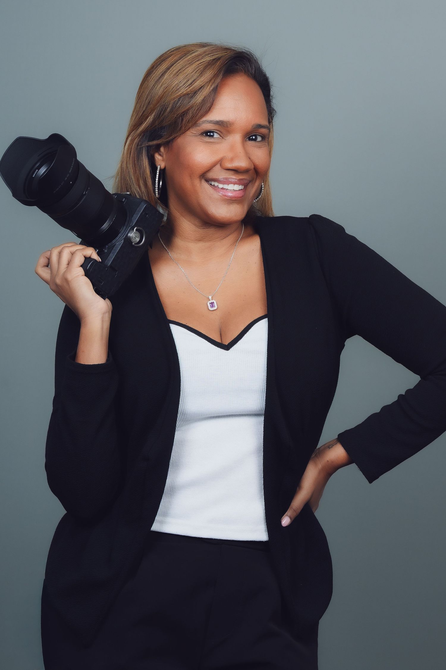 Professional photographer in business attire holding camera against gray background.