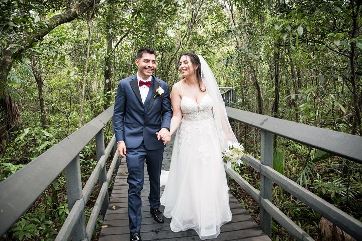 Newlyweds walk along wooden boardwalk surrounded by lush green forest by FBM Studios in Ft Lauderdale Fl.
