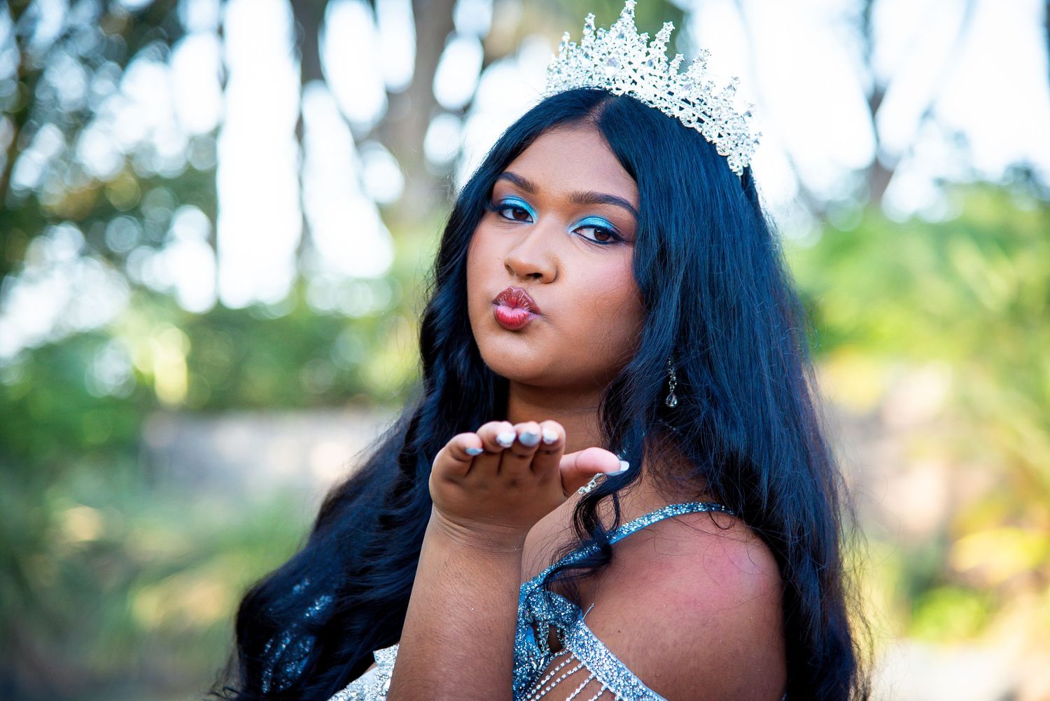 Woman with long black hair poses outdoors in a sparkly silver dress making different expressions.