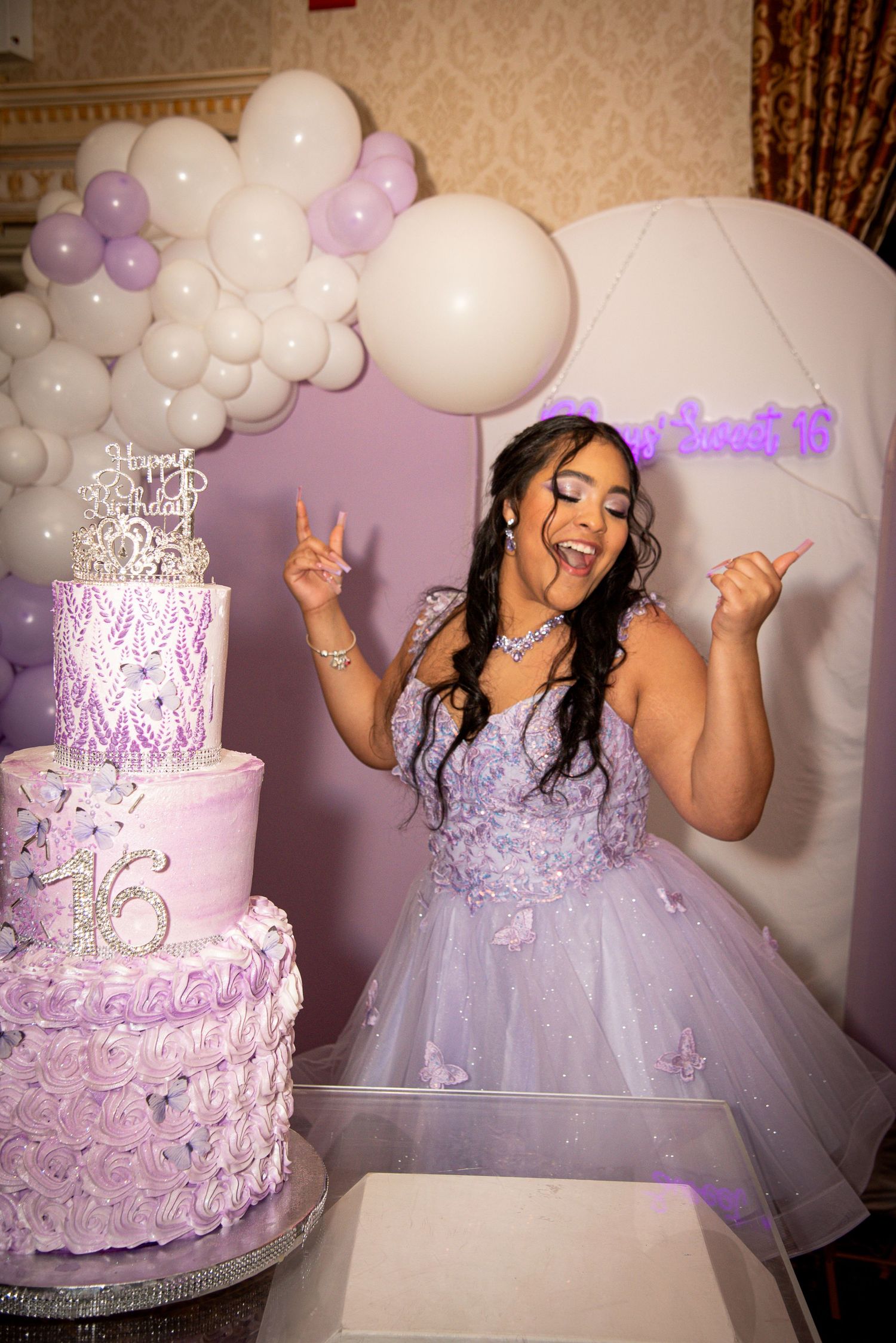 Girl in lavender ball gown celebrates Sweet 16 beside a purple tiered cake with balloons in the background by FBM Studios in Fort Lauderdale
