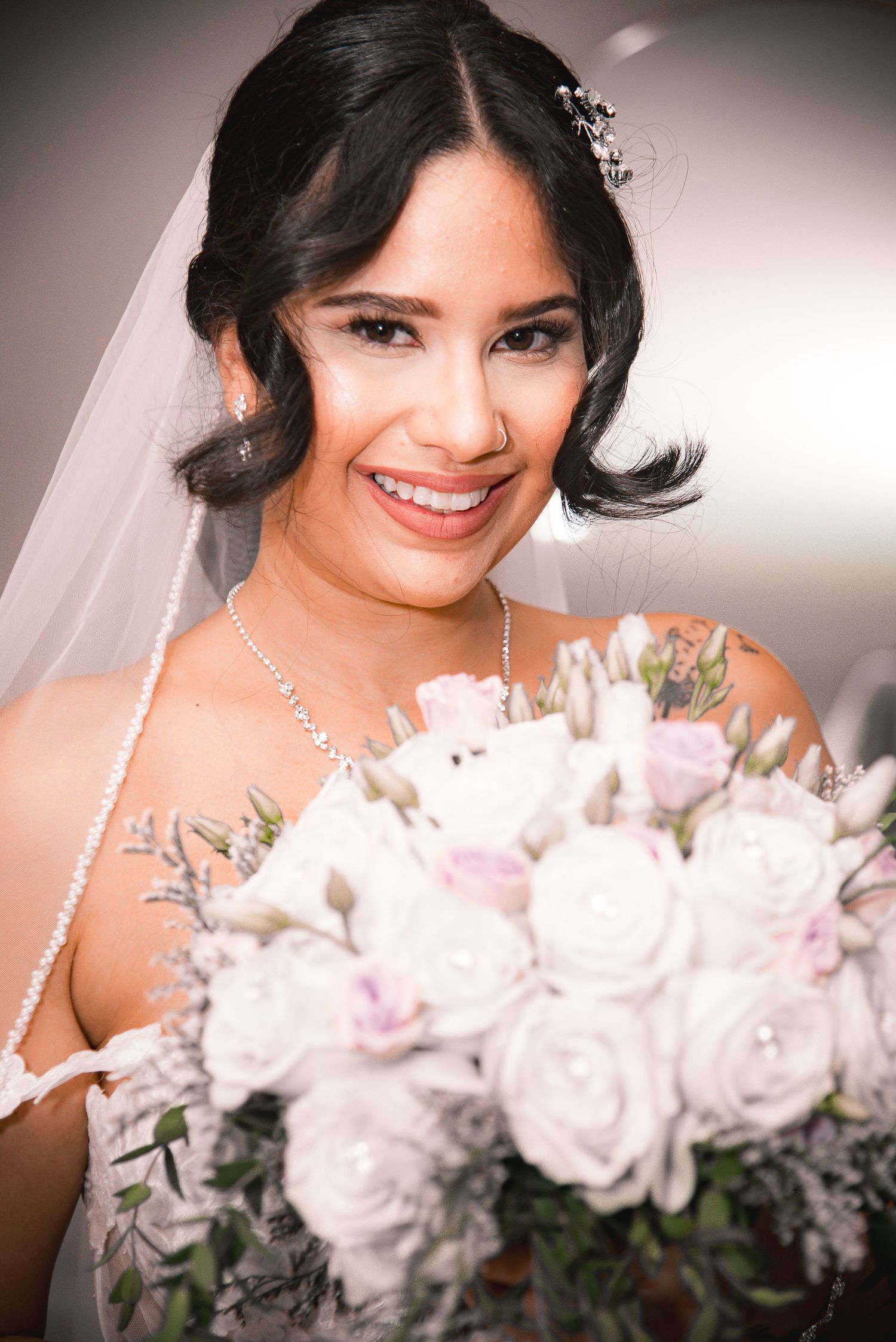 Smiling bride in white gown and veil holds bouquet of white and pink roses on her wedding day.
