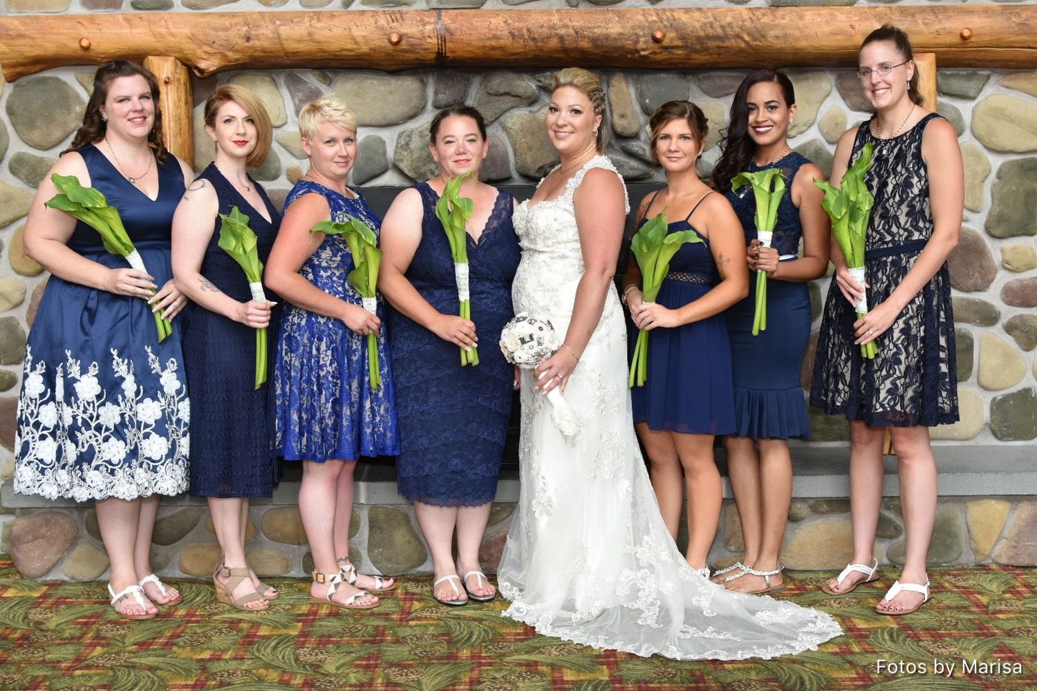 Wedding party members in navy blue and white dresses sit together on a rustic log bench for outdoor photos.