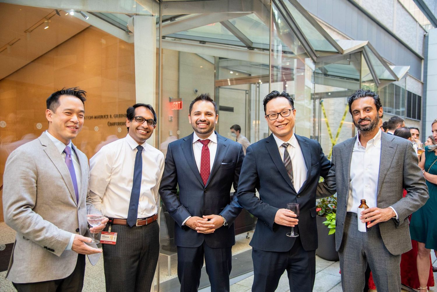 Five professional men smiling and posing together at a formal networking event in a modern building.
