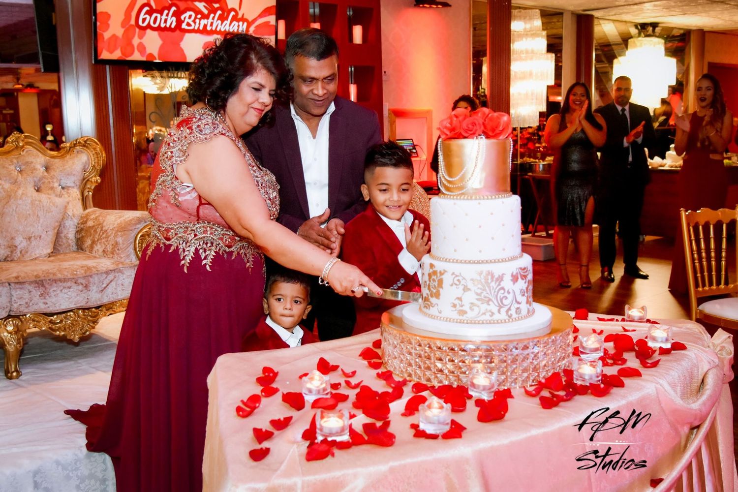 A wedding cake decorated with red rose petals being cut at an elegant reception with burgundy and red decor by FBM Studios in Ft Lauderdale