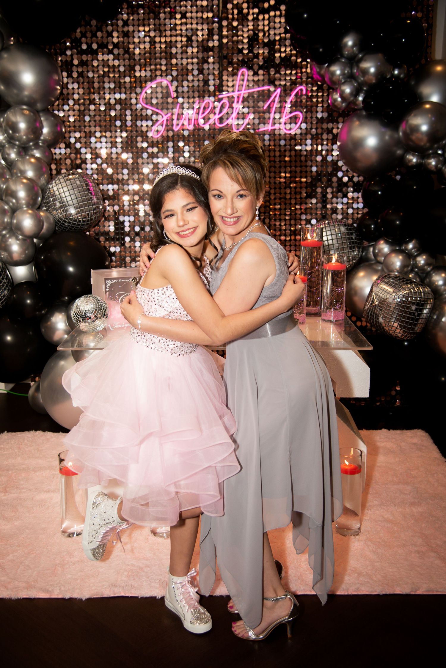 A young girl in a pink tulle dress hugs a woman in gray at a Sweet 16 party with balloon decor by FBM Studios in Fort Lauderdale Florida.