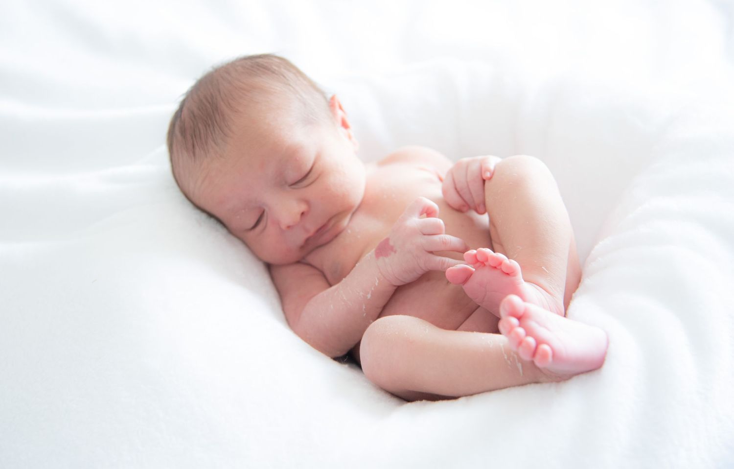Sleeping newborn baby wrapped in white blanket lying on soft white bedding in peaceful slumber.