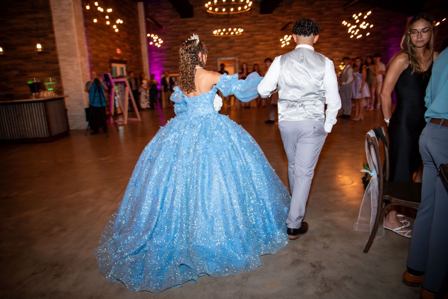 A girl in a blue ball gown dances with a partner in white at a quinceañera celebration.