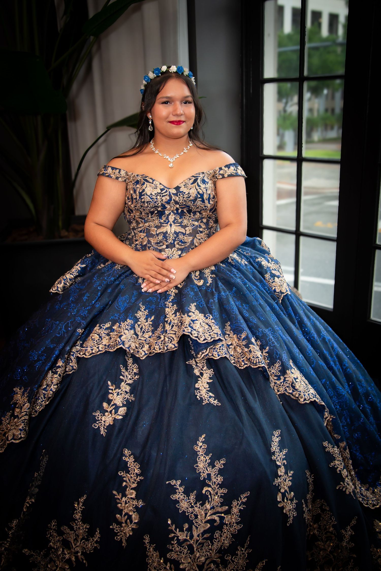 Young woman in elegant navy blue quinceanera ball gown with gold embroidered details posing for formal portrait.