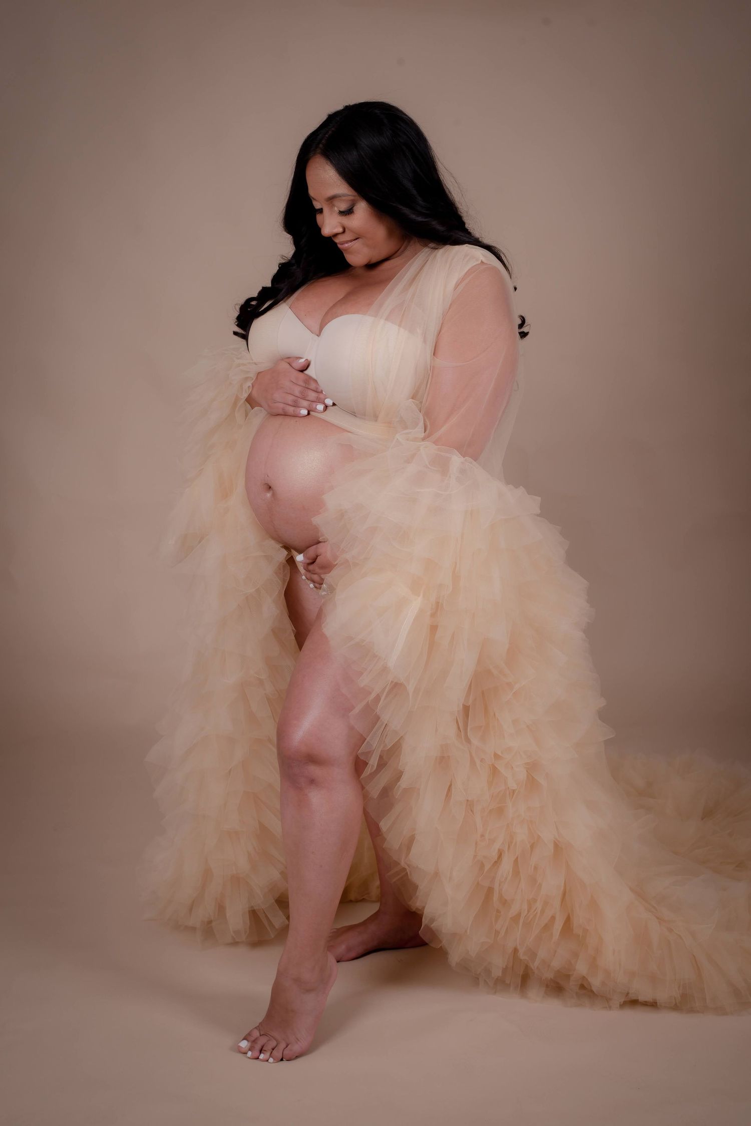 Artistic maternity photoshoot featuring soft peach tulle dress against neutral backdrop.