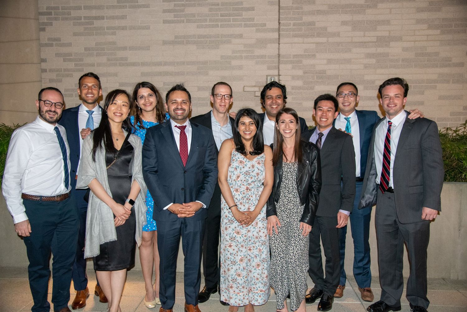 A diverse group of professionals in formal attire smiling together at an indoor event or celebration.