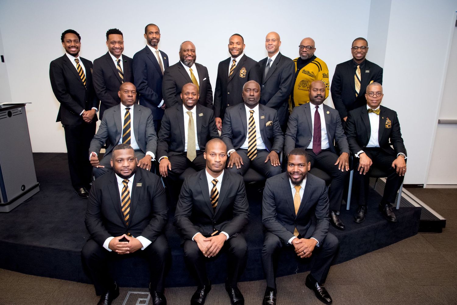 Group of professionally dressed men posing for a formal group photo in suits and ties at an official event.