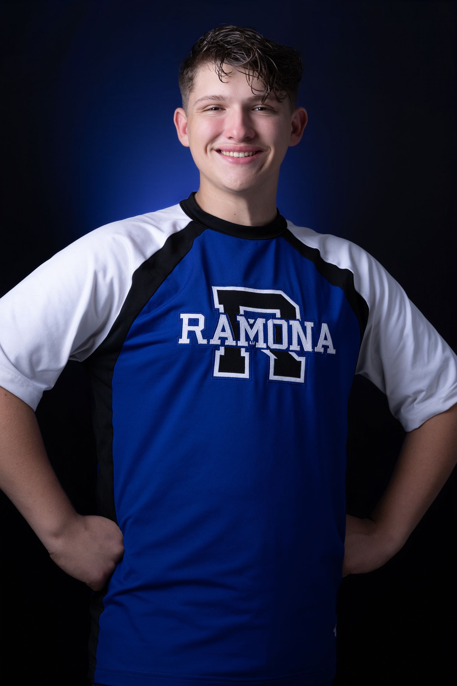Smiling teen boy in blue Ramona athletic shirt posing against a dark blue background.