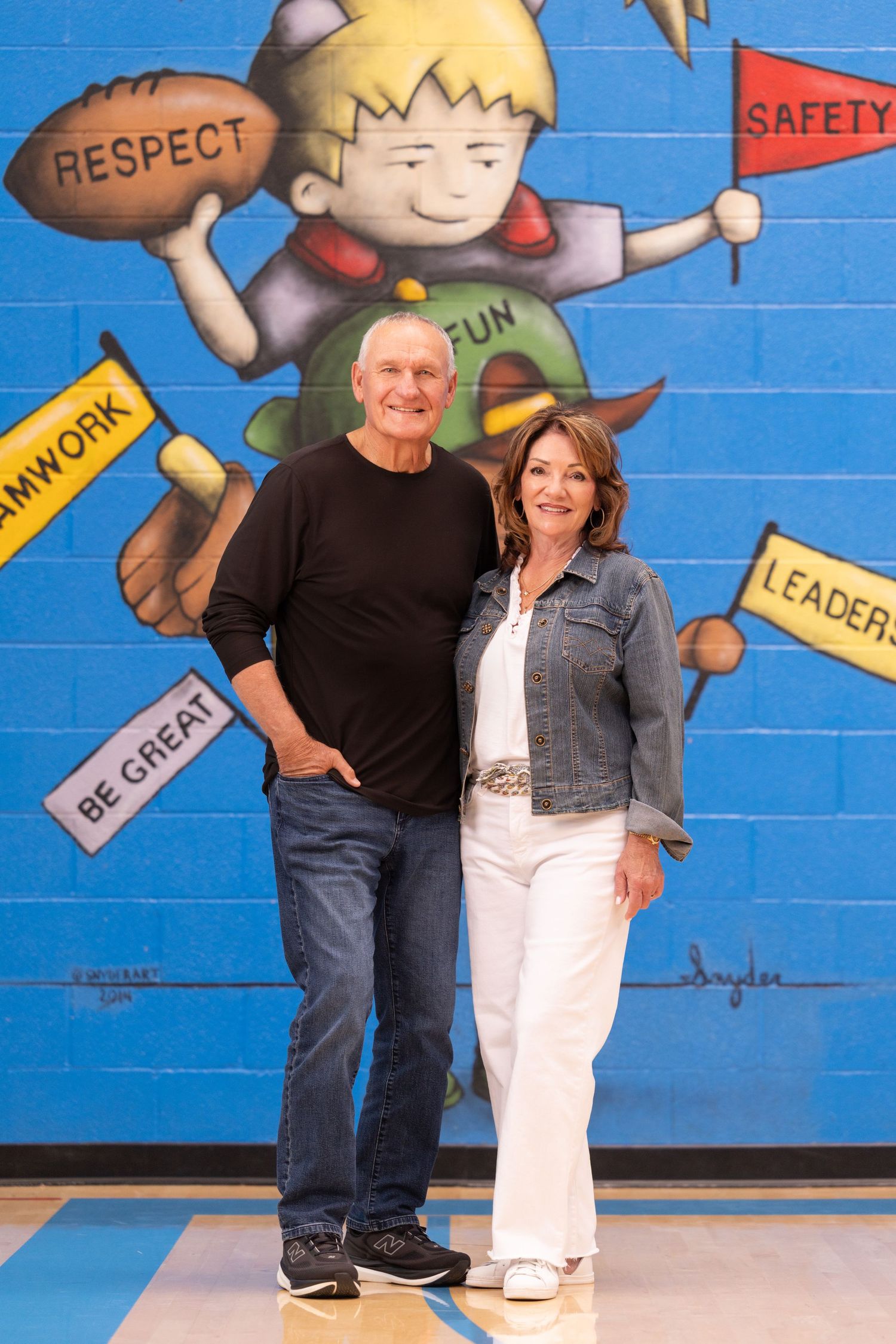 Couple smiling in front of colorful school mural with words Respect, Safety, Teamwork, and Leadership.