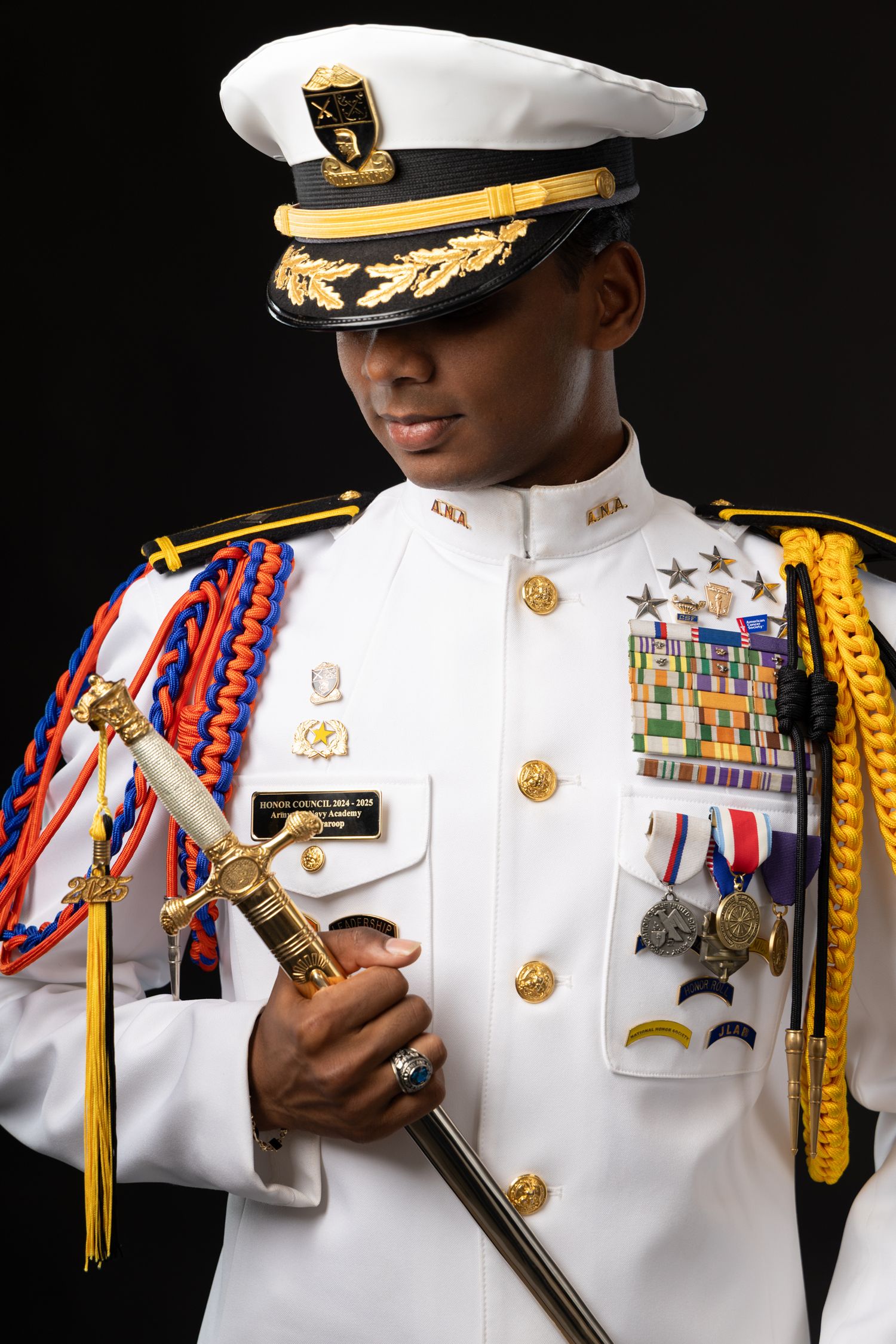 Military officer in white dress uniform with medals, aiguillettes, and sword on black background.