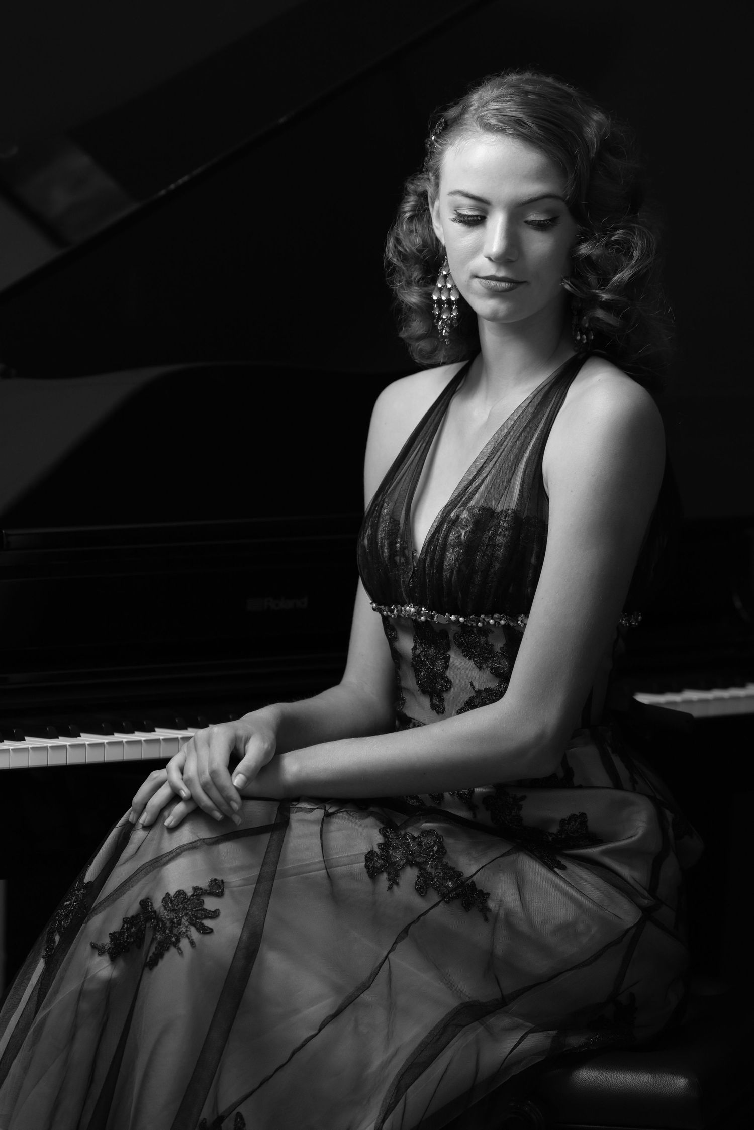 Elegant woman in embroidered gown seated at grand piano in black and white portrait photography.