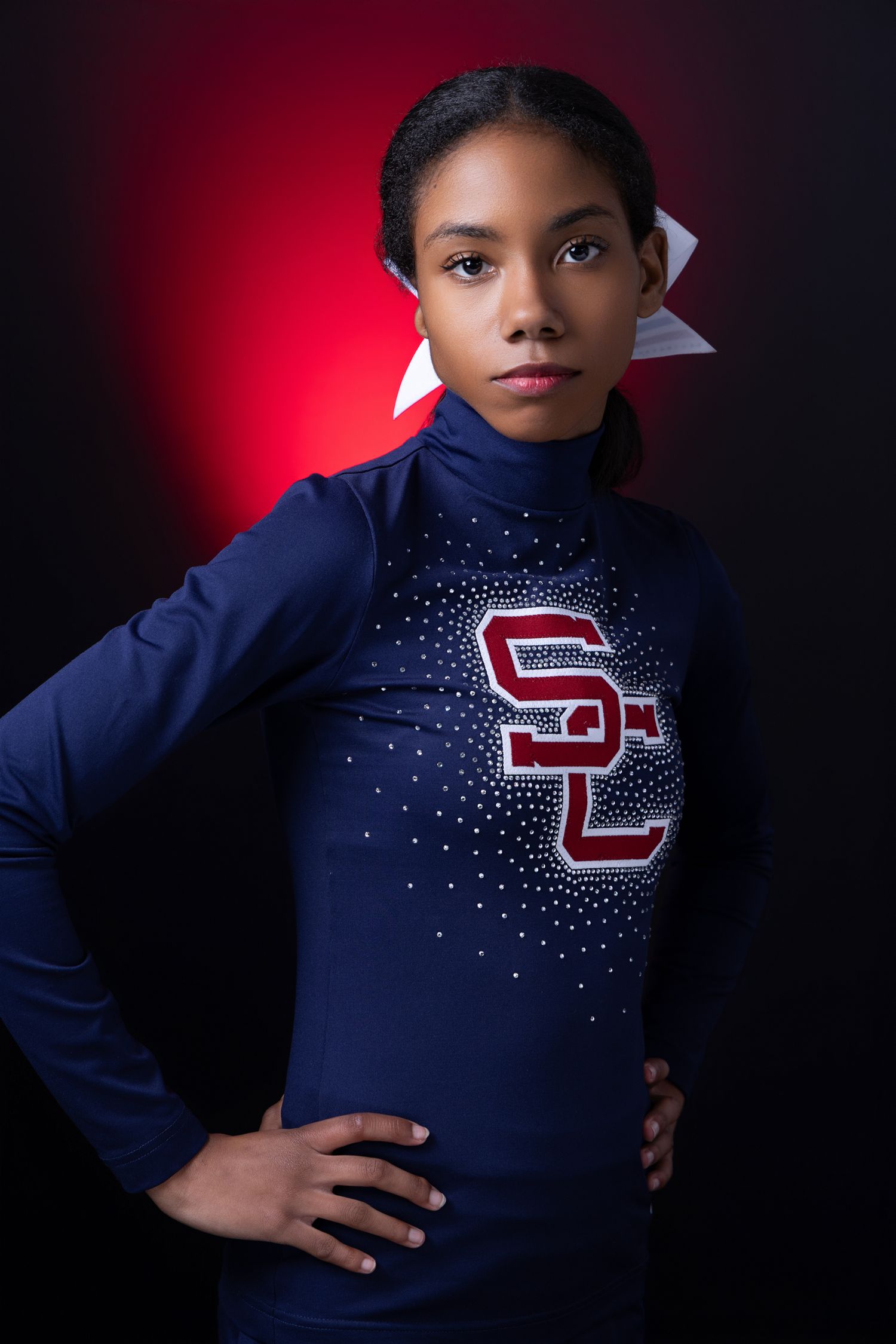 Young female athlete in navy SL uniform posing confidently against a red and black background.
