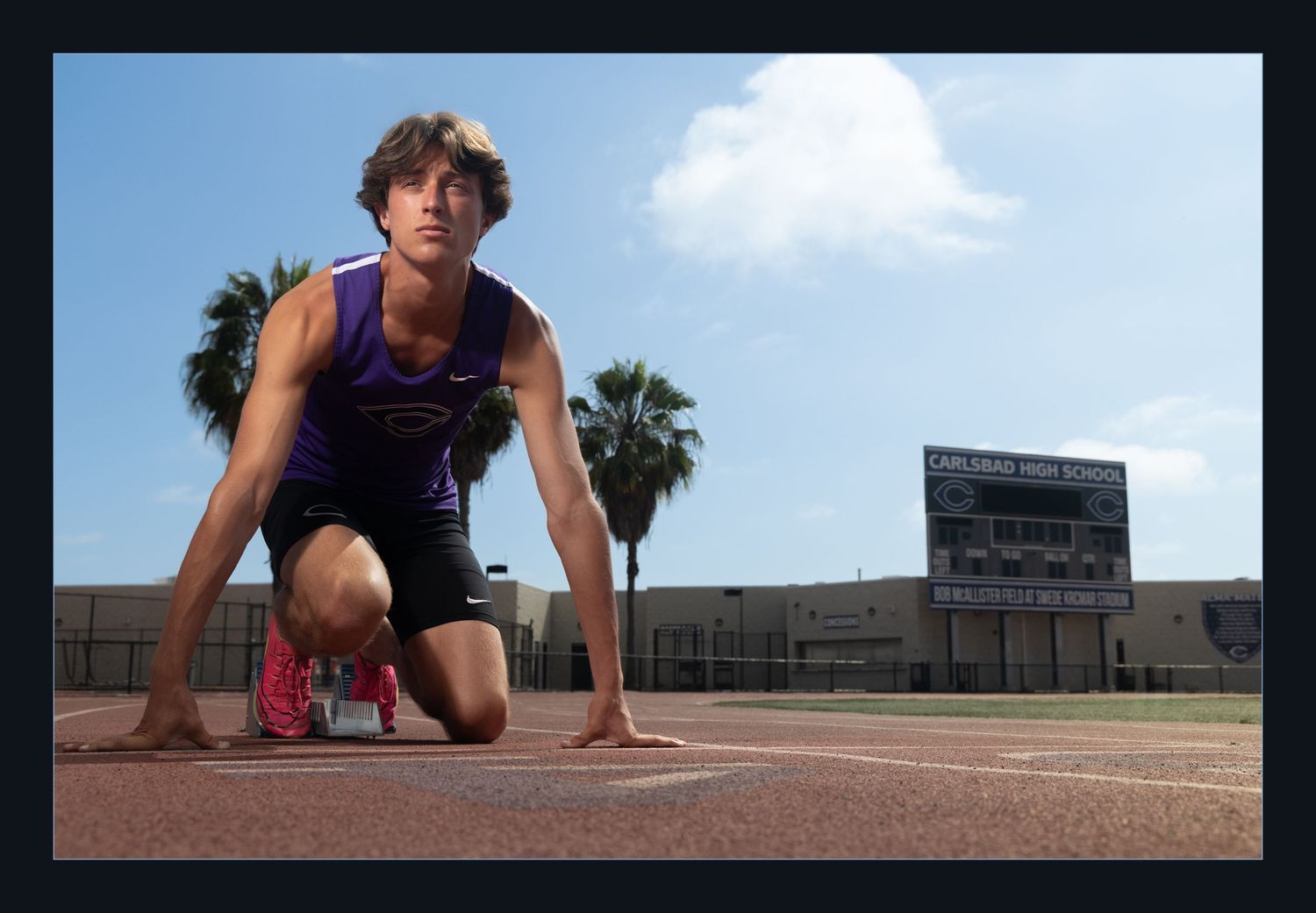 Male track athlete in starting position on school running track under blue sky.
