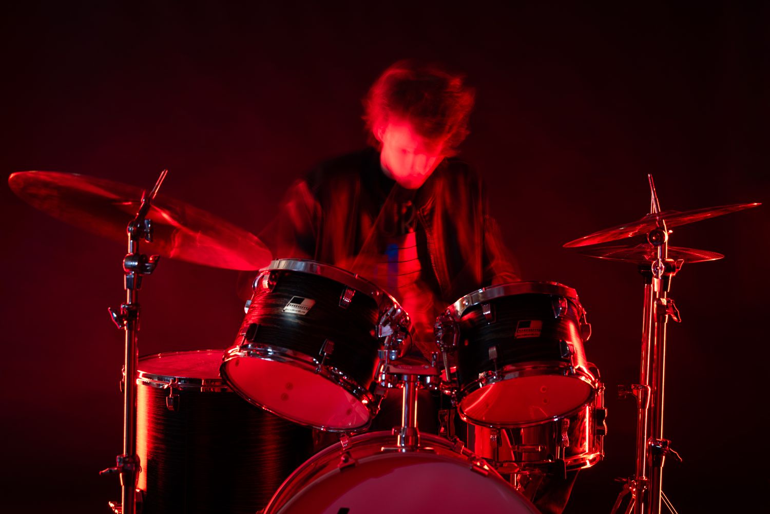 Drummer performing on stage bathed in dramatic red lighting with a full drum kit setup.