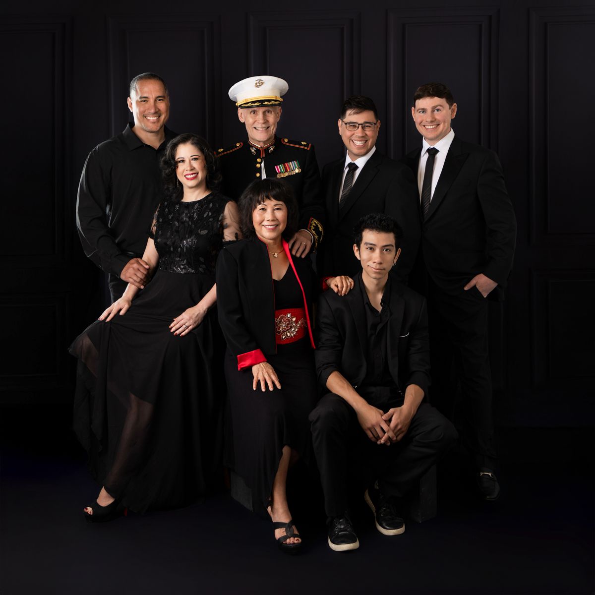 Family portrait in formal attire with a US Marine in dress uniform against a dark background.