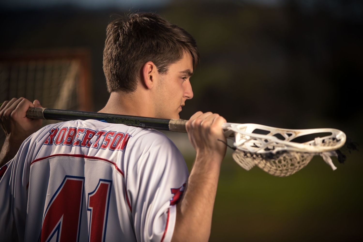 Young lacrosse player in jersey number 41 holding a lacrosse stick over his shoulder outdoors.