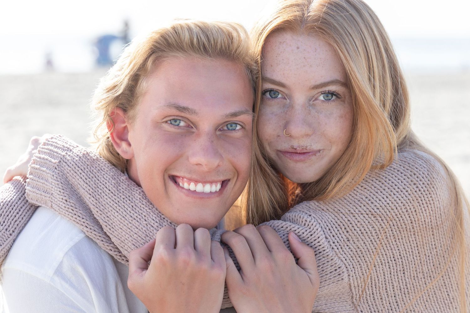 Young couple embracing and smiling at the beach, woman with freckles hugging man from behind.