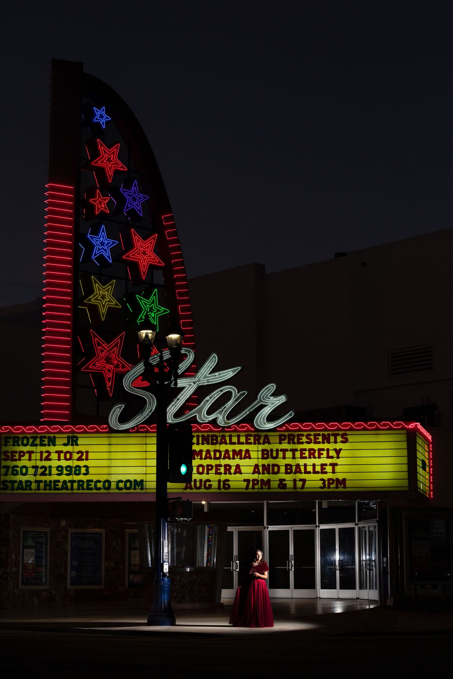 Woman in red gown stands before the illuminated Star Theatre marquee at night with colorful neon stars.