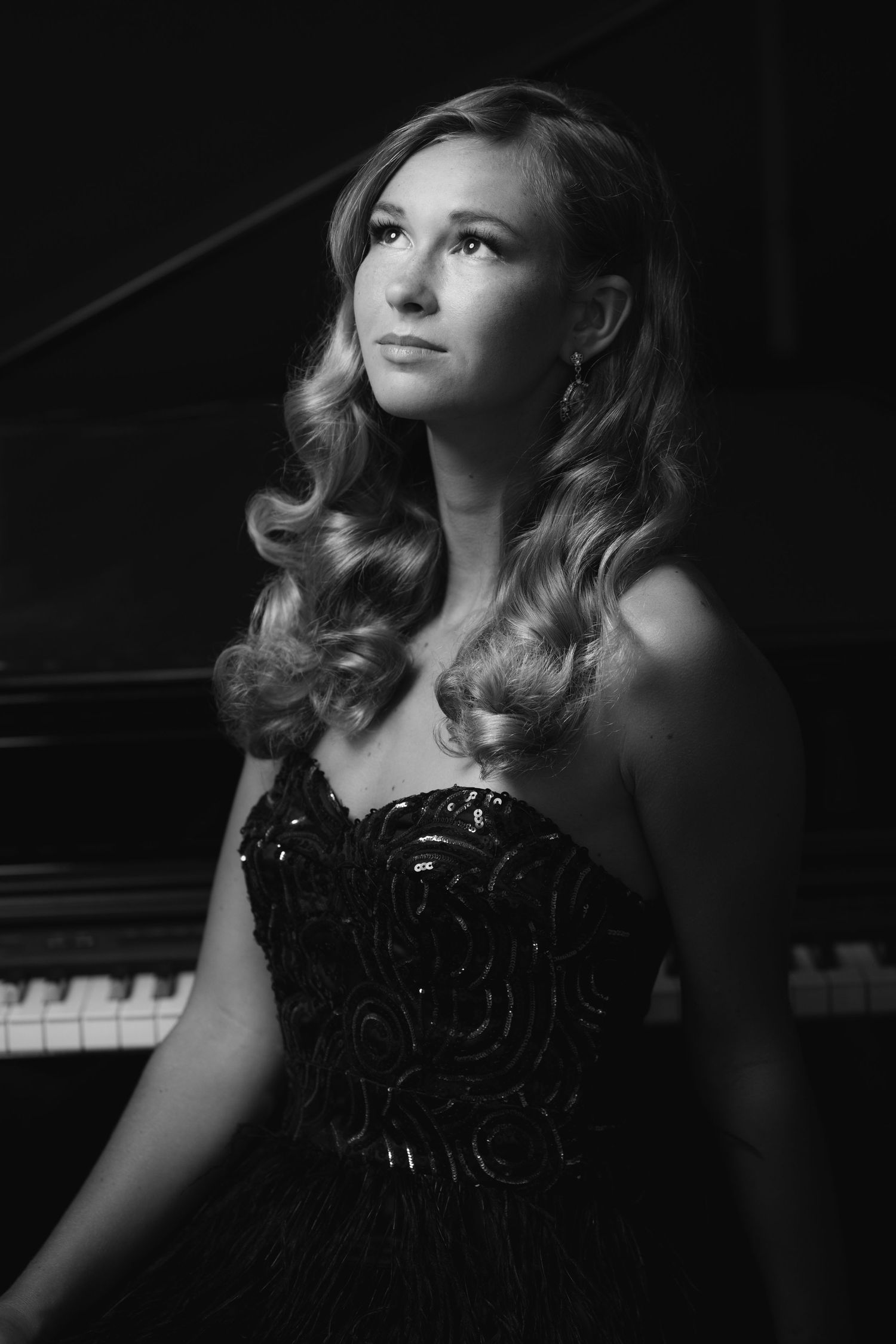 Black and white portrait of elegant woman in sequined gown posing near grand piano keys.