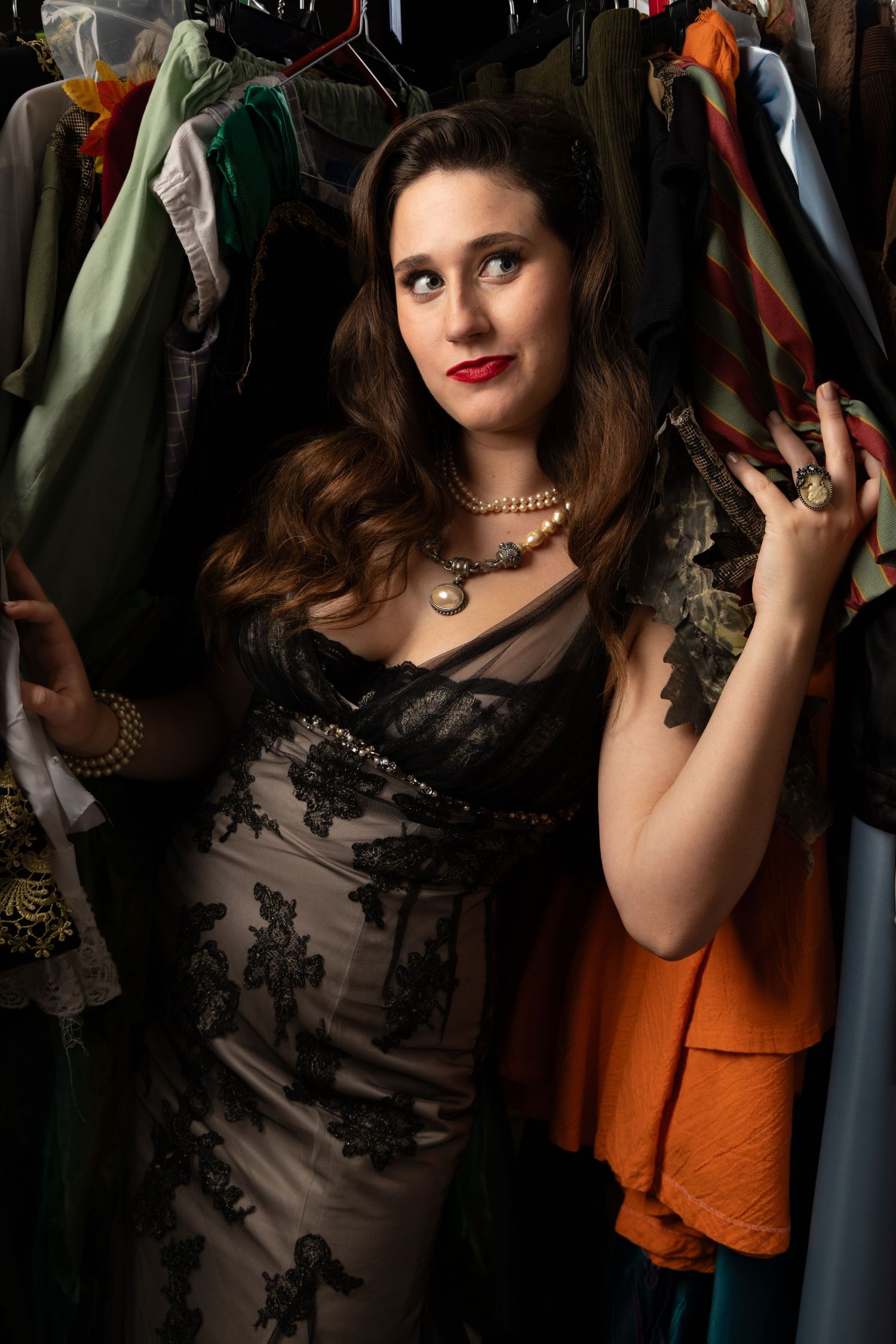 Woman in black lace dress browsing clothes on a rack, wearing pearl necklace and vintage jewelry.