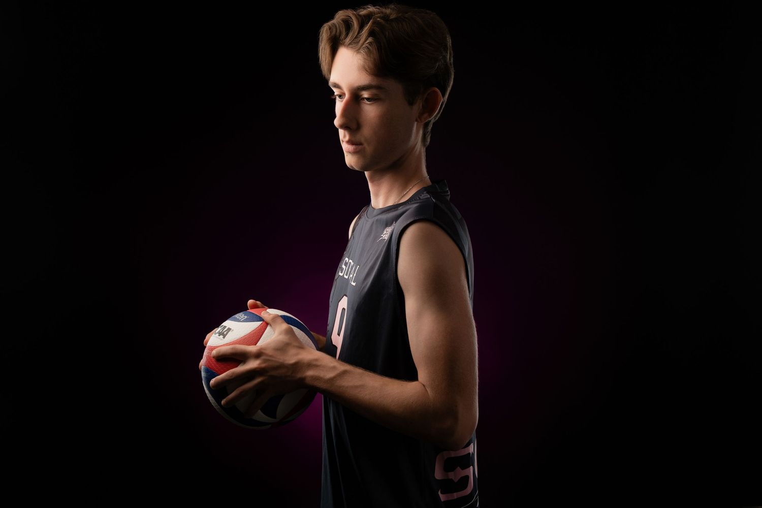 Young male athlete holding a volleyball in dramatic studio lighting against a dark background.