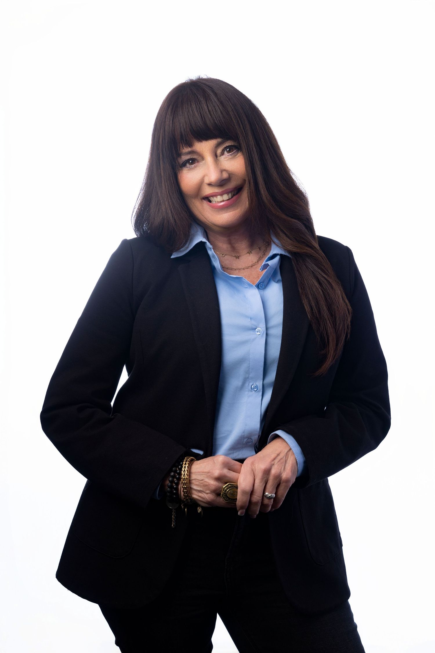 Professional businesswoman in black blazer and blue shirt smiling confidently against white background.