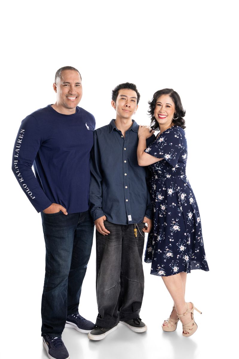 Family of three smiling together in coordinating blue outfits against white background for a professional portrait.