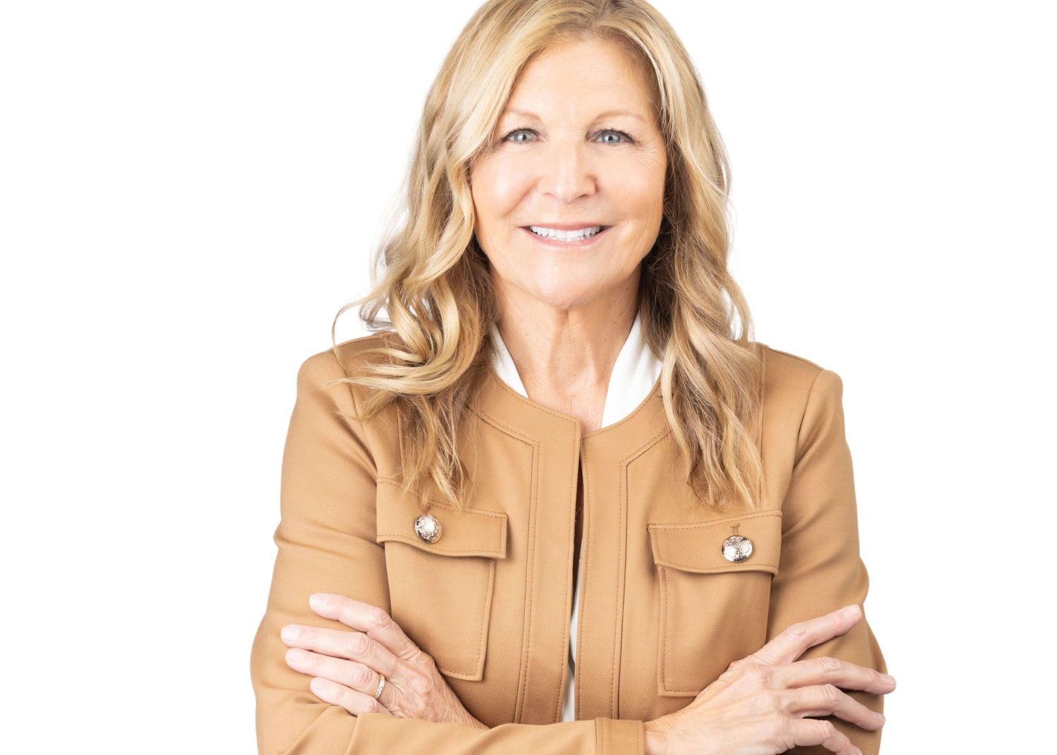 Confident professional woman with blonde hair in tan blazer smiling with arms crossed on white background.