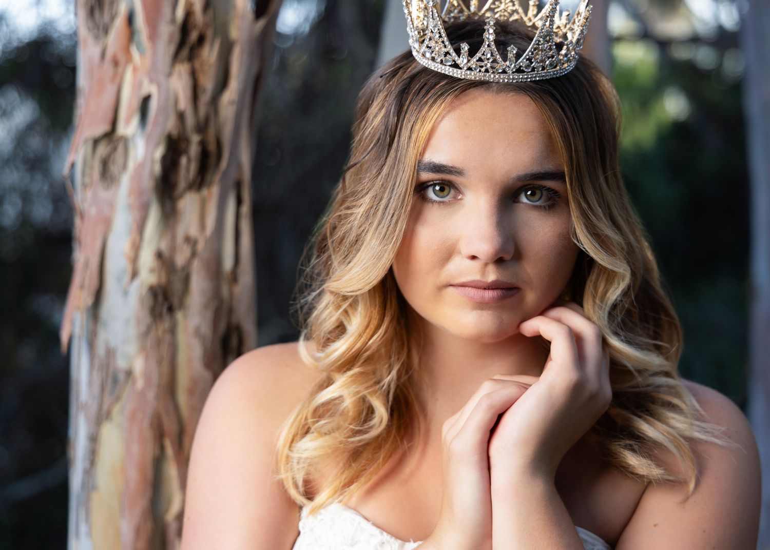 Close-up portrait of a young woman wearing a gold crown with soft waves and natural makeup outdoors.